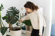 © PintoArt - woman listens to music at home while watering plants