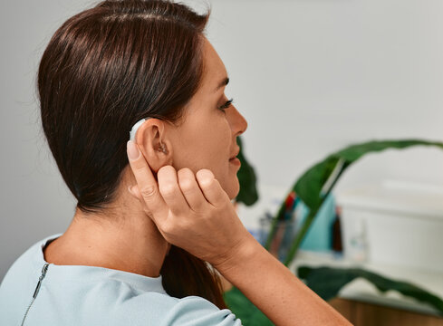 Adult woman with hearing aid behind the ear can hear sounds. Hearing loss treatment concept and hearing solutions for people with deafness
