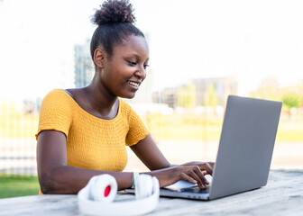 young african american woman working on her laptop in a city park, student preparing exam, concept of working, studying, blogger and influencer on remote