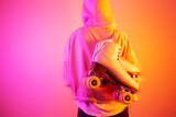 Teenager girl carrying classic leather roller skates on pink and orange background
