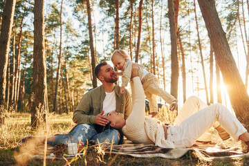 Woman is laying down. Happy family of father, mother and little daughter is in the forest