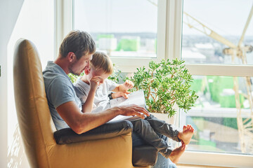 Sitting with book. Beautiful sunlight. Father and son is indoors at home together