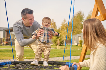 Man putting joyful kid on swing and watching woman