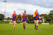 © Austockphoto - three women footballers jogging across football oval in red and blue uniforms