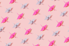 Creative pattern made of paper crane origami figures on pastel pink background. Minimal flat lay visual.