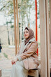 © Sarbinaz Mustafina - Muslim woman in beige coat and headscarf. Stylish Muslim woman in the park. A girl sitting on a bench