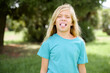 Caucasian little kid girl wearing blue T-shirt standing outdoors sticking tongue out happy with funny expression. Emotion concept.