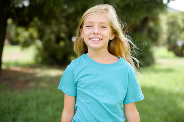 Wall Mural - Caucasian little kid girl wearing blue T-shirt standing outdoors with a happy and cool smile on face. Lucky person.