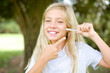 © Roquillo - Caucasian little kid girl wearing white T-shirt standing outdoors holding an invisible aligner and pointing at it. Dental healthcare and confidence concept.