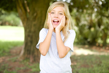 Wall Mural - Caucasian little kid girl wearing whiteT-shirt standing outdoors Pleasant looking cheerful, Happy reaction