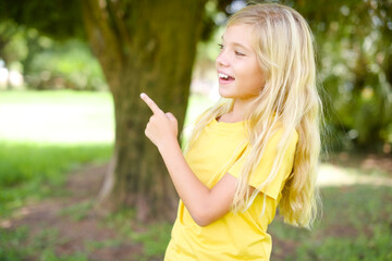 Wall Mural - beautiful Caucasian little kid girl wearing yellow T-shirt standing outdoors glad cheery demonstrating copy space look novelty