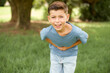 beautiful Caucasian little kid boy wearing blue T-shirt standing outdoors smiling and laughing hard out loud because funny crazy joke with hands on body.