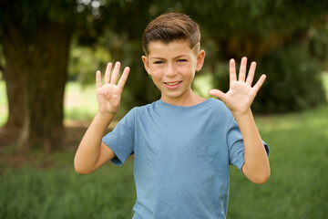 Wall Mural - beautiful Caucasian little kid boy wearing blue T-shirt standing outdoors showing and pointing up with fingers number nine while smiling confident and happy.