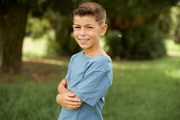 Wall Mural - beautiful Caucasian little kid boy wearing blue T-shirt standing outdoors  happy face smiling with crossed arms looking at the camera. Positive person.