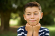 © Roquillo - Caucasian little kid boy wearing stripped T-shirt standing outdoors holds hands under chin, glad to hear heartwarming words from stranger