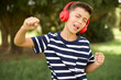Carefree beautiful Caucasian little kid boy wearing stripped T-shirt  thick beard and toothy smile raises arms dances carefree moves with rhythm of music listens music from playlist via headphones