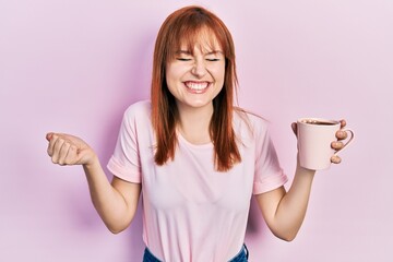 Poster - Redhead young woman drinking a cup coffee screaming proud, celebrating victory and success very excited with raised arm