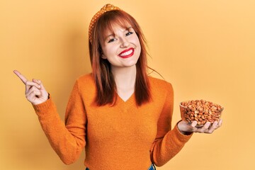 Poster - Redhead young woman holding peanuts smiling happy pointing with hand and finger to the side