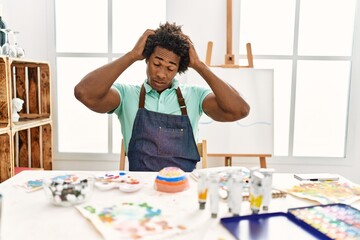 Canvas Print - Young african american man sitting on the table at art studio suffering from headache desperate and stressed because pain and migraine. hands on head.