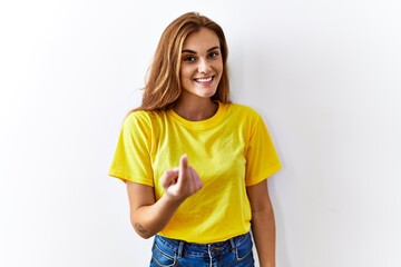 Wall Mural - Young brunette woman standing over isolated background beckoning come here gesture with hand inviting welcoming happy and smiling