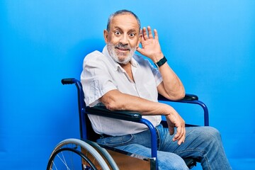 Poster - Handsome senior man with beard sitting on wheelchair smiling with hand over ear listening an hearing to rumor or gossip. deafness concept.