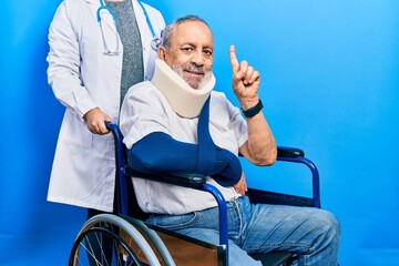 Canvas Print - Handsome senior man with beard sitting on wheelchair with neck collar with a big smile on face, pointing with hand finger to the side looking at the camera.