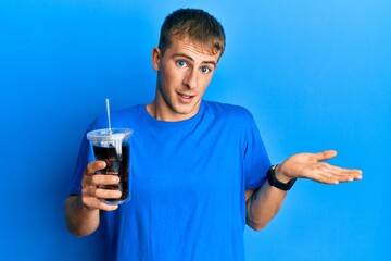 Wall Mural - Young caucasian man drinking glass of soda beverage celebrating achievement with happy smile and winner expression with raised hand