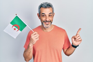 Sticker - Handsome middle age man with grey hair holding algeria flag smiling happy pointing with hand and finger to the side