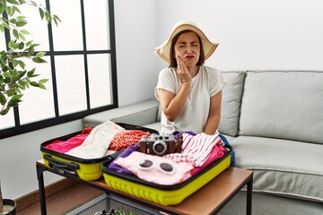 Poster - Beautiful middle age hispanic woman packing summer clothes in suitcase touching mouth with hand with painful expression because of toothache or dental illness on teeth. dentist