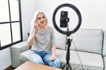 Sticker - Young caucasian woman recording vlog tutorial with smartphone at home showing and pointing up with fingers number three while smiling confident and happy.