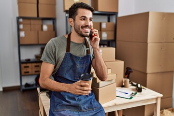 Young hispanic man business worker talking on the smartphone drinking coffee at storehouse