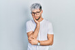 Young hispanic man with modern dyed hair wearing white t shirt and glasses thinking looking tired and bored with depression problems with crossed arms.