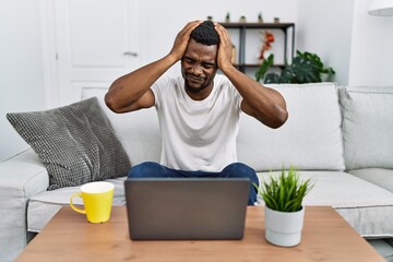 Wall Mural - Young african man using laptop at home suffering from headache desperate and stressed because pain and migraine. hands on head.