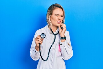 Poster - Beautiful young blonde doctor woman holding stethoscope touching mouth with hand with painful expression because of toothache or dental illness on teeth. dentist concept.