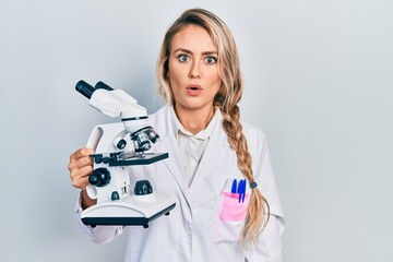 Sticker - Beautiful young blonde woman holding microscope scared and amazed with open mouth for surprise, disbelief face