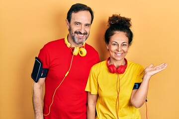 Poster - Middle age couple of hispanic woman and man wearing sportswear and arm band smiling cheerful presenting and pointing with palm of hand looking at the camera.