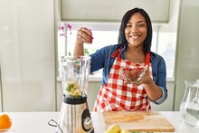 Hispanic Brunette Woman Preparing Fruit Smoothie With Raspberries At The Kitchen