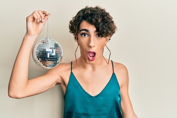 Canvas Print - Young hispanic gay holding shiny disco ball scared and amazed with open mouth for surprise, disbelief face