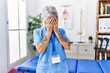 © Krakenimages.com - Middle age grey-haired woman wearing physiotherapist uniform at medical clinic with sad expression covering face with hands while crying. depression concept.