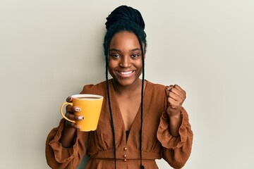 Sticker - African american woman with braided hair drinking a cup coffee screaming proud, celebrating victory and success very excited with raised arm