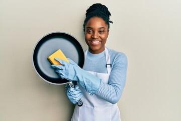 Poster - African american woman with braided hair wearing apron holding scourer washing pan smiling with a happy and cool smile on face. showing teeth.