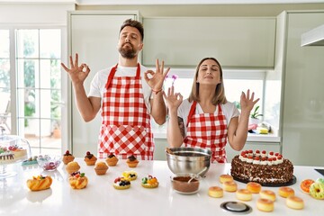 Wall Mural - Young couple cooking pastries at the kitchen relax and smiling with eyes closed doing meditation gesture with fingers. yoga concept.