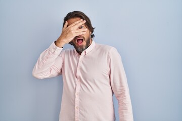 Sticker - Handsome middle age man wearing elegant shirt background peeking in shock covering face and eyes with hand, looking through fingers with embarrassed expression.