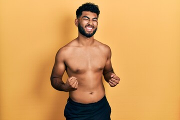 Wall Mural - Arab man with beard wearing swimwear shirtless excited for success with arms raised and eyes closed celebrating victory smiling. winner concept.