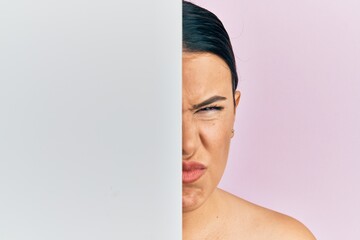 Sticker - Beautiful brunette woman holding blank empty banner covering half face skeptic and nervous, frowning upset because of problem. negative person.