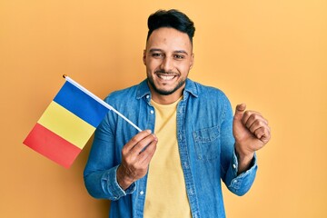 Young arab man holding romania flag screaming proud, celebrating victory and success very excited with raised arm