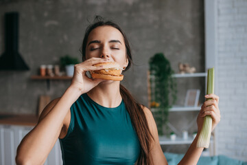 Wall Mural - Fit woman in sportwear eating burger in the kitchen after workout. Weight loss concept. Food concept.