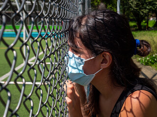 Young Brunette Woman Using a Blue Mask is Looking Through the Mesh of the Soccer Field