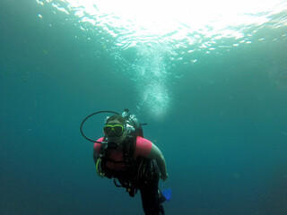 Young woman practices the sport scuba diving with oxygen tank equipment, visor, fins, relaxes and enjoys the bottom of the crystal clear water next to large branches and trunks
