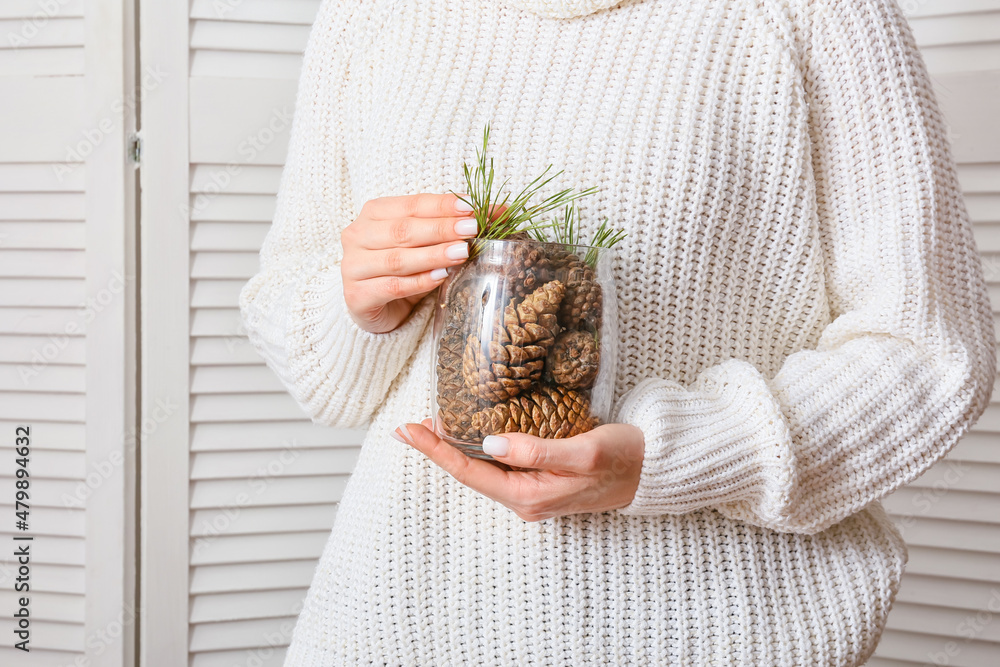 Woman holding jar with pine cones indoors, closeup